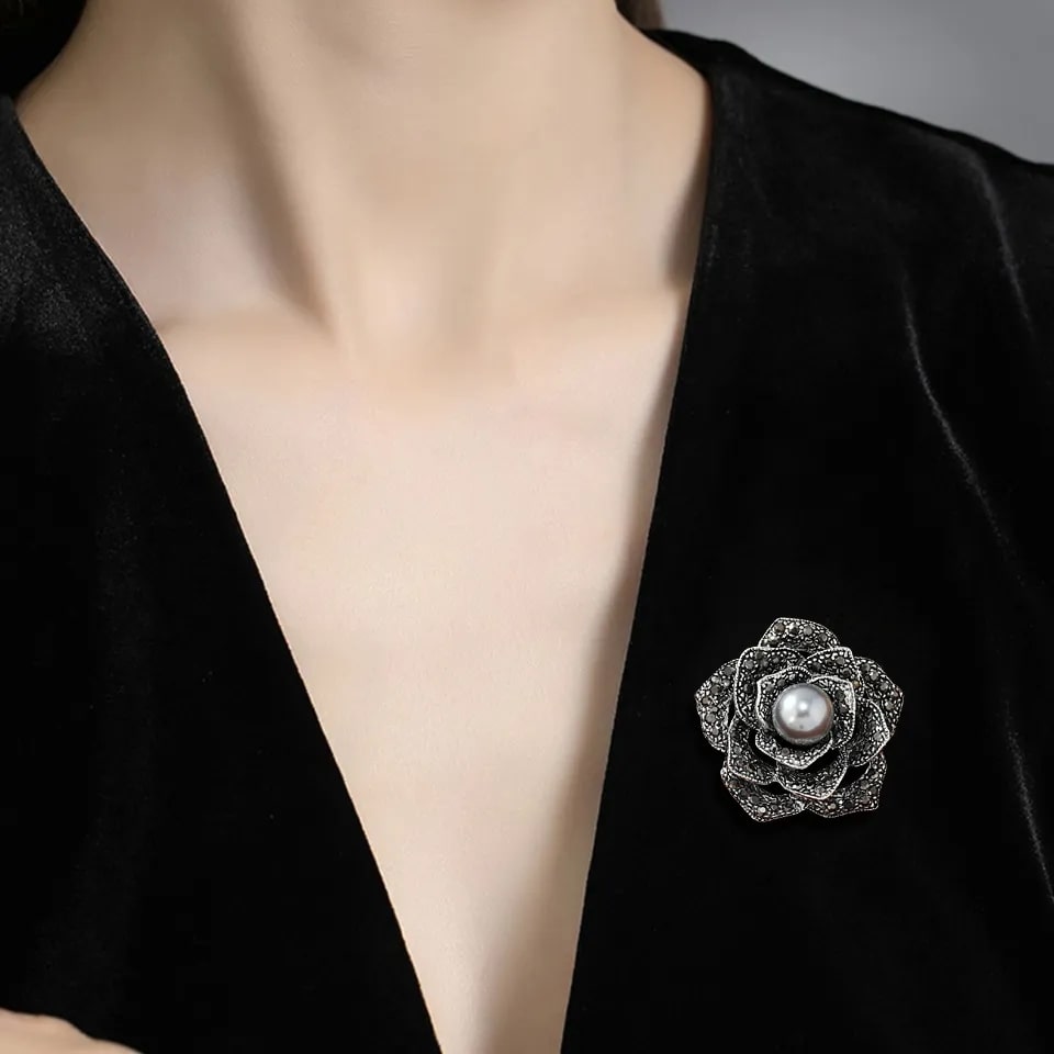 A woman wearing a black velvet dress and a silver rose brooch. The brooch features a silver pearl surrounded by blooming petals adorned with dazzling rhinestones