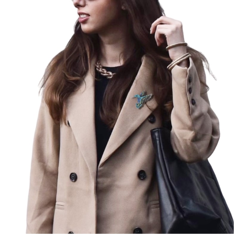 beige coat and black top on a woman complemented by a turquoise rhinestone hummingbird brooch