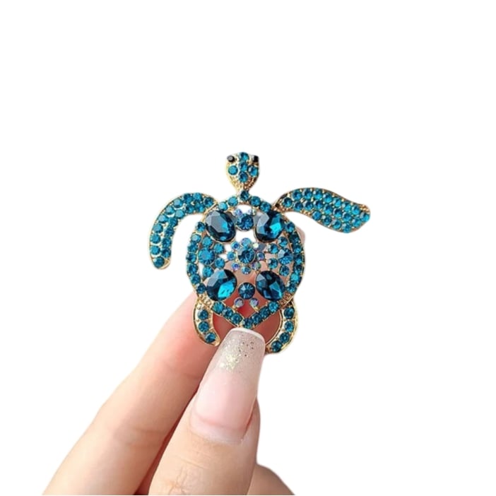 a hand holding a sparkly blue turtle brooch with intricate details