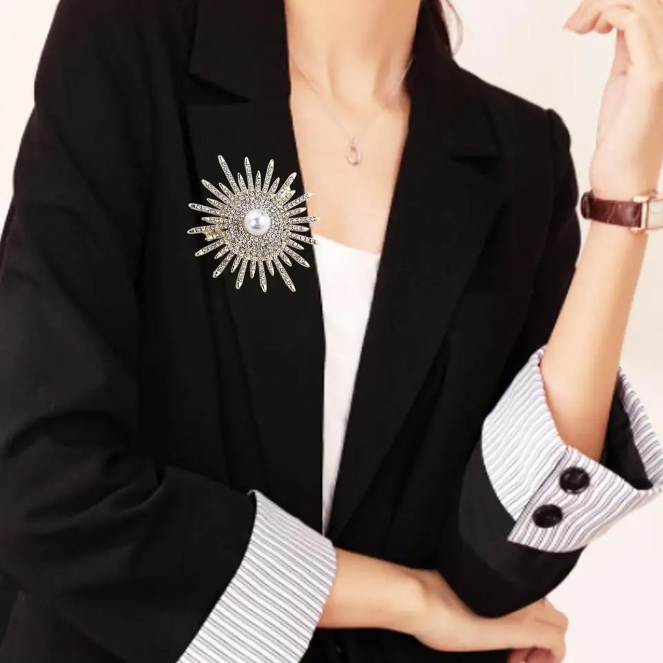woman in black blazer and white shirt with sparkling rhinestone sun rays brooch, featuring pearl center and dazzling rhinestones