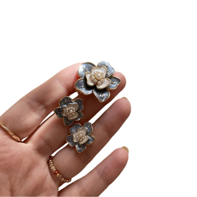 Person holding gray and white French Enamel Flower earrings with Daffodil and Buttercup-like flowers, gold edges, and pearl centers