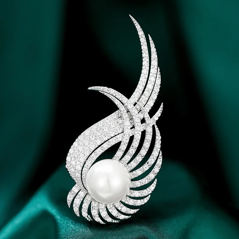 a stunning pearl and diamond brooch on a green cloth, a fashionable wing design inlaid with cubic zirconia.